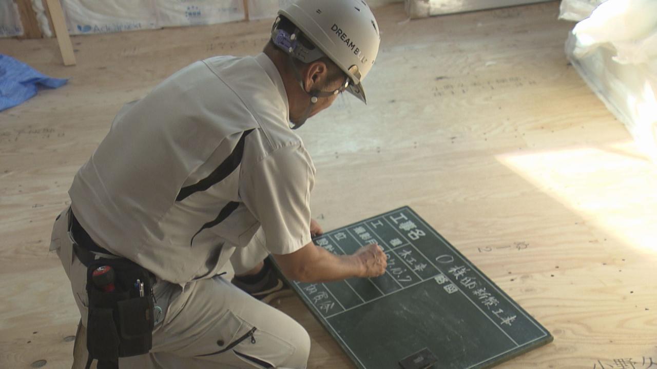 もうこの時代には戻りたくないと言いながら黒板に文字を書き入れる現場監督